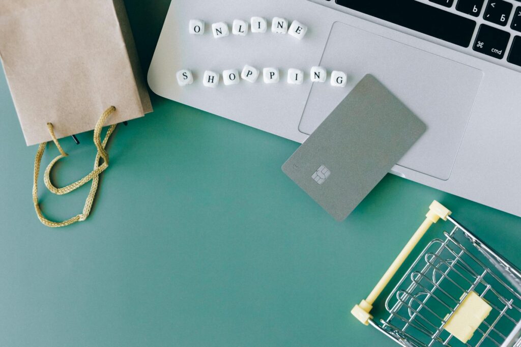 Flat lay of online shopping essentials with laptop, card, and shopping cart.