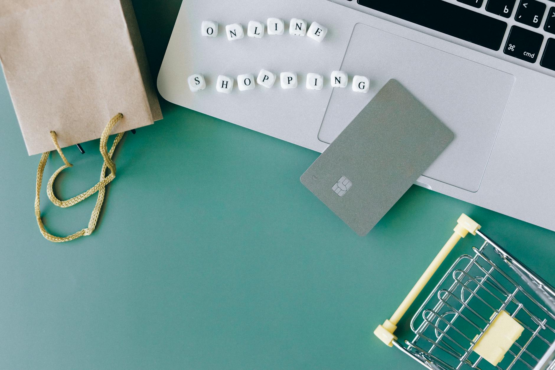 Flat lay of online shopping essentials with laptop, card, and shopping cart.
